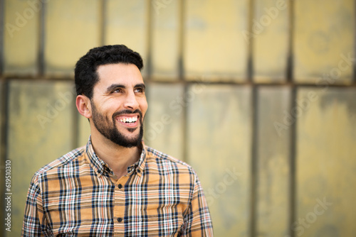 Handsome young arabic man standing against yellow wall looking away and smiling