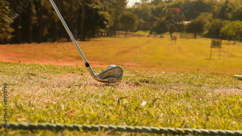 Visão de um taco de golfe e uma bola de golfe no tee em um campo aberto em um dia de sol. 