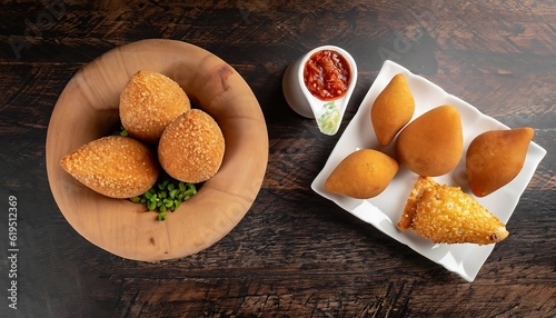 On a dark wooden background, traditional Brazilian snacks coxinha and quibe are displayed photo