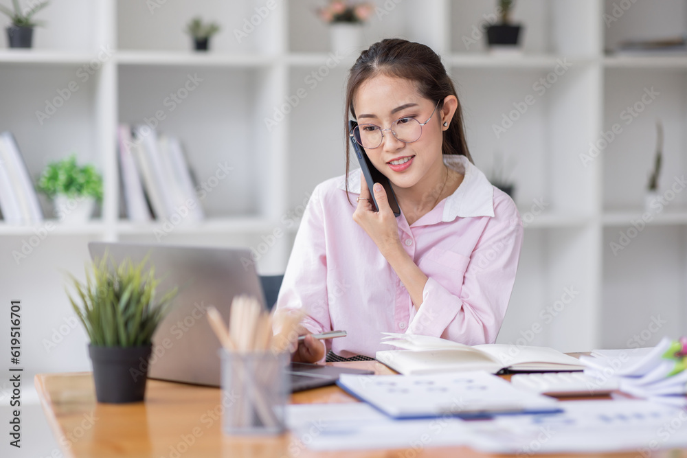 Cheerful business Asian woman freelancer wear glasses making telephone call share good news about project working in office workplace, business finance concept. Cheerful business Asian woman freelancer wear glasses making telephone call share good news about project working in office workplace, business finance concept.