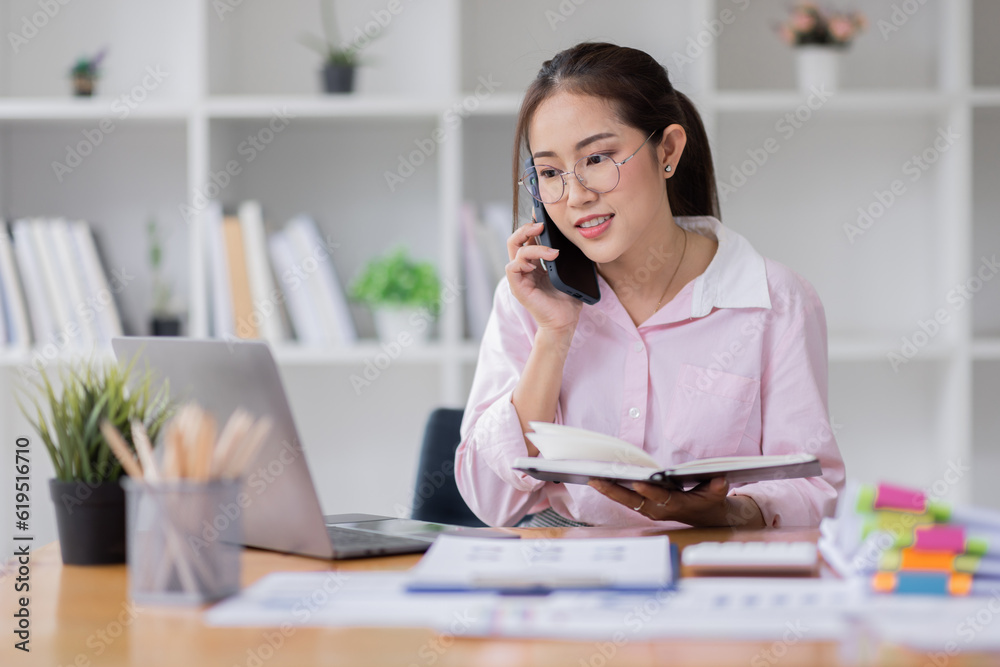 Obraz premium Cheerful business Asian woman freelancer wear glasses making telephone call share good news about project working in office workplace, business finance concept.