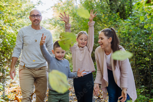 Happy family having fun with a foliage in autumn forest.