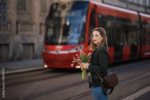 Portrait of young woman in city with bouquet of tulips.