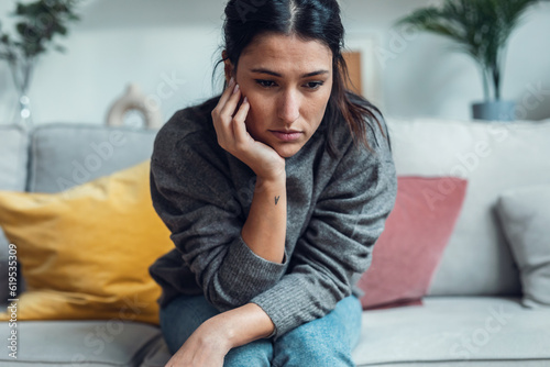 Worried depressed woman thinking while sitting on sofa in the living room at home. photo