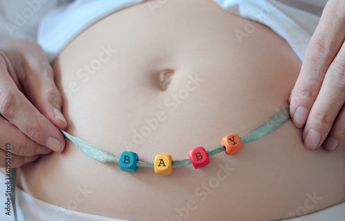 belly of a pregnant woman close-up  the word baby from wooden cubes  the concept of happy motherhood and enjoy pregnancy