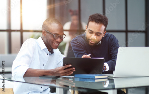 colleagues sitting together at a table in a modern office talking and using a laptop