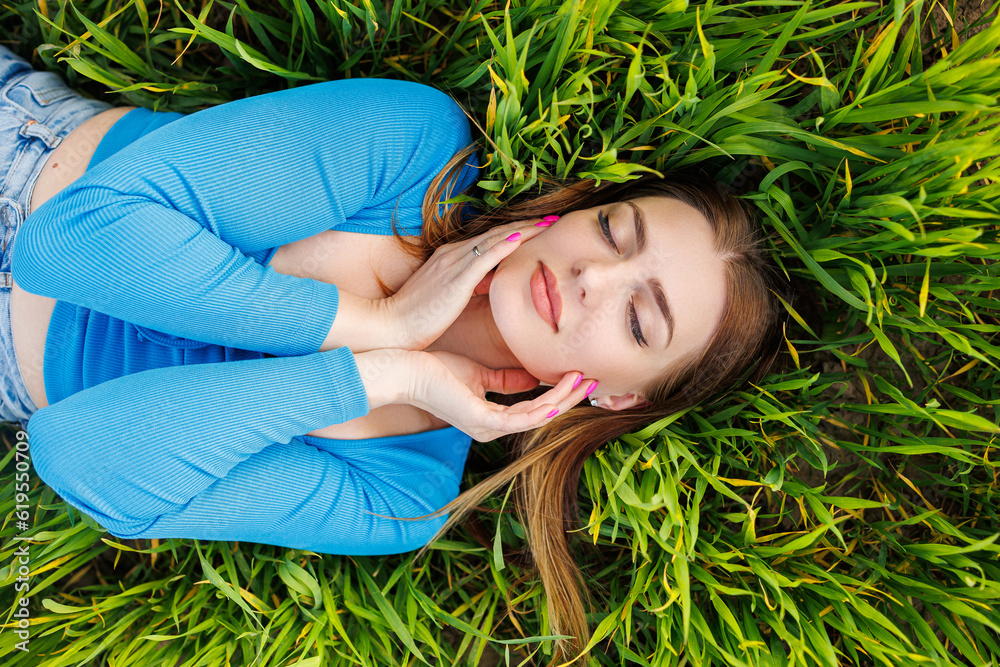 Happy young woman lies on green grass and enjoys nature. Smiling attractive woman in green grass Happy young woman lies on green grass and enjoys nature. Smiling attractive woman in green grass