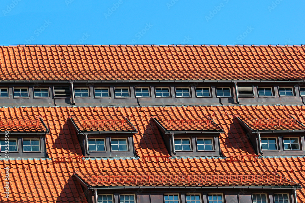 Attic windows in orange tiled roof against blue sky background