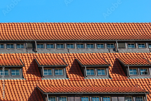 Attic windows in orange tiled roof against blue sky background