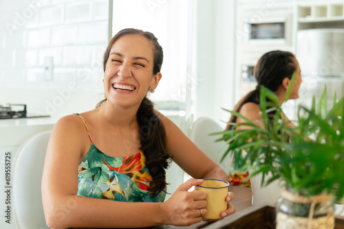 happy woman laughing and drinking coffee at living room table