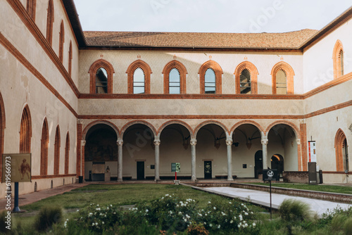 Milan, Italy- May 13, 2023: Inner courtyard view,  Castello Sforzesco ancient monument, green lawn of courtyard, blue sky white clouds background, © Евгения Жигалкина