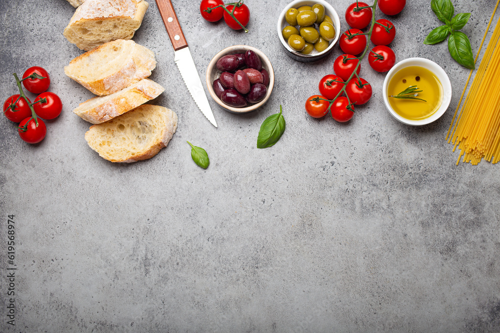 Food composition with sliced ciabatta, olives, olive oil, spaghetti, fresh basil, cherry tomatoes on gray concrete stone rustic background top view, copy space. Italian cuisine concept
