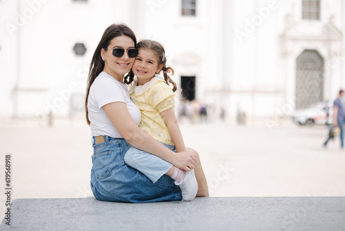 Portrait of mom and daughter sits on stone bench and hug each other