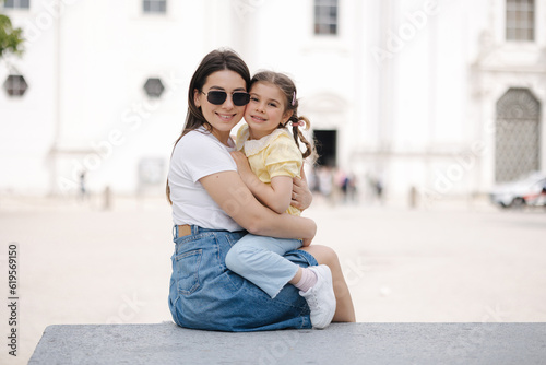 Portrait of mom and daughter sits on stone bench and hug each other