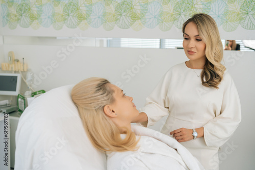 Portrait of professional gynecologist having consultation with young pregnant woman in white bathrobe lying on medical couch at gynecological clinic. Concept of healthy motherhood.