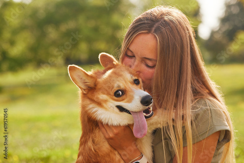 Photography young girl hugging and kissing a cheerful Welsh Corgi and in the park in sunny w