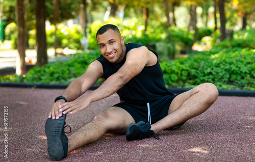 Cheerful handsome african american athlete man in sportswear stretching legs for jogging