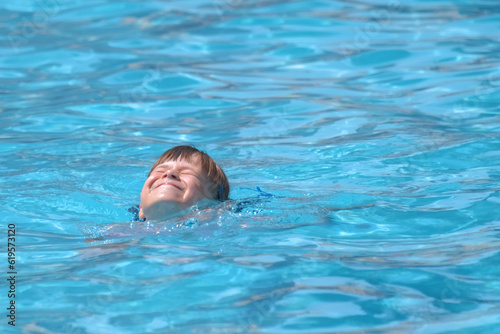 Child girl learns to swim. Funny face with closed eyes on bright blue rippled water surface