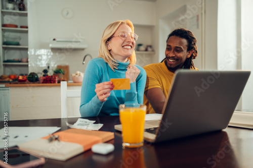 A happy multiracial couple in love is sitting at home and shopping online  using a laptop and credit card.