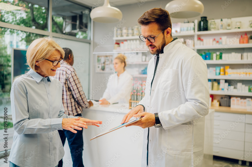 Portrait of a male pharmacist helping a senior woman customer in pharmacy