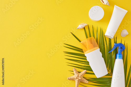 Skincare routine for summer vacation. Top view composition of sunblock cosmetic mockups, tropical leaf, seashells, starfish on yellow background with empty space for advert or text