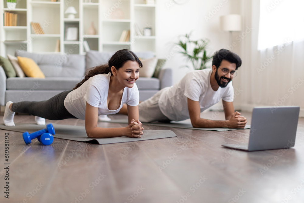 Training At Home. Sporty indian couple doing plank exercise with laptop Training At Home. Sporty indian couple doing plank exercise with laptop