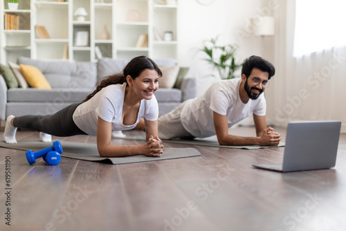 Training At Home. Sporty indian couple doing plank exercise with laptop