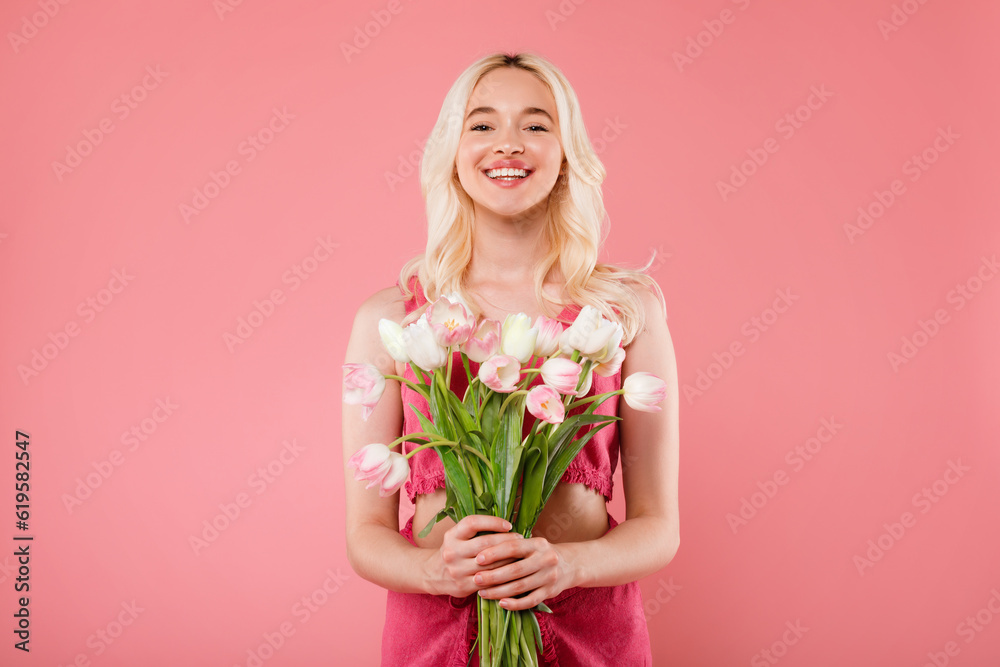 Happy charming blonde lady holding bouquet of flowers, enjoy women day or birthday, smiling at camera, pink background