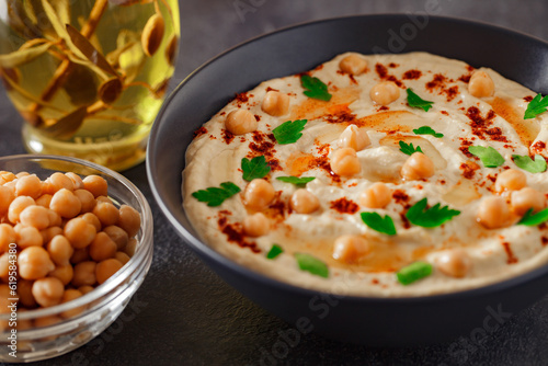 Hummus with chickpeas, oil, spices and herbs in bowl on dark background, selective focus