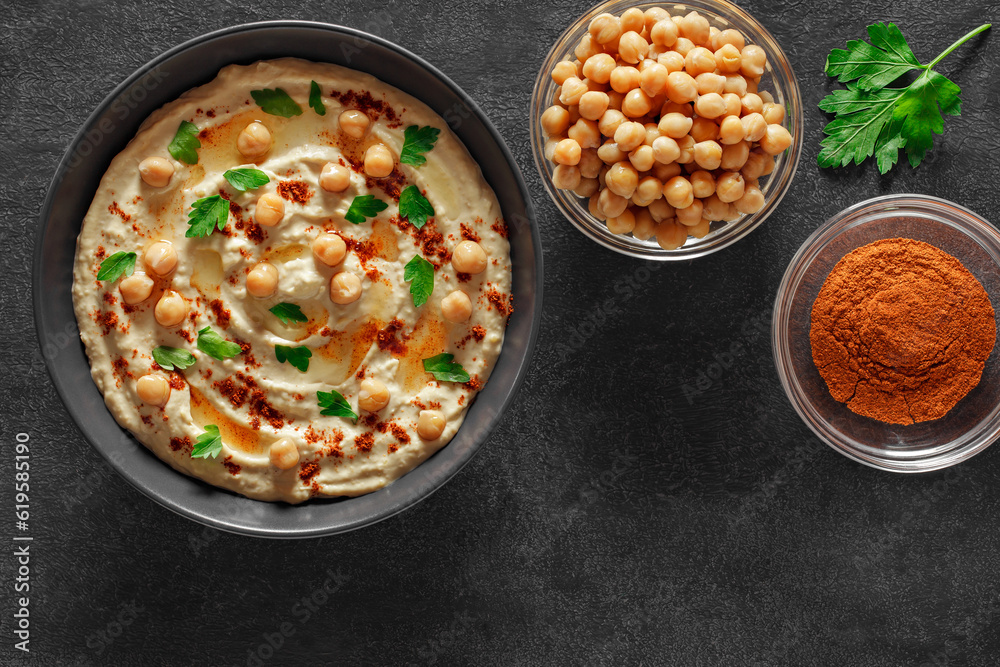 Hummus with chickpeas, oil, spices and green parsley in bowl on dark background, top view.