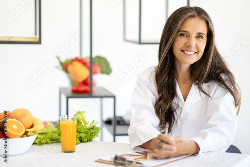 Happy adult european woman doctor nutritionist in white coat with organic fruits and vegetables photo