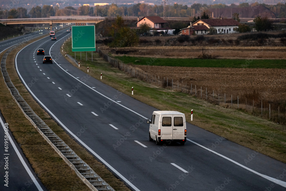 White delivery van on the highway. White modern delivery small shipment cargo courier van moving fast on motorway road to city urban suburb. The world's best transport of goods. White delivery van on the highway. White modern delivery small shipment cargo courier van moving fast on motorway road to city urban suburb. The world's best transport of goods.