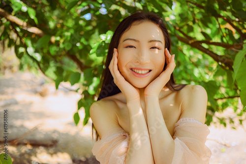 Close up outdoor portrait Beautiful young Chinese Asian woman perfect skin posing outside sunny summer day green foliage. Natural facial treatment. Cosmetology  skin care and spa. Fragnance concept