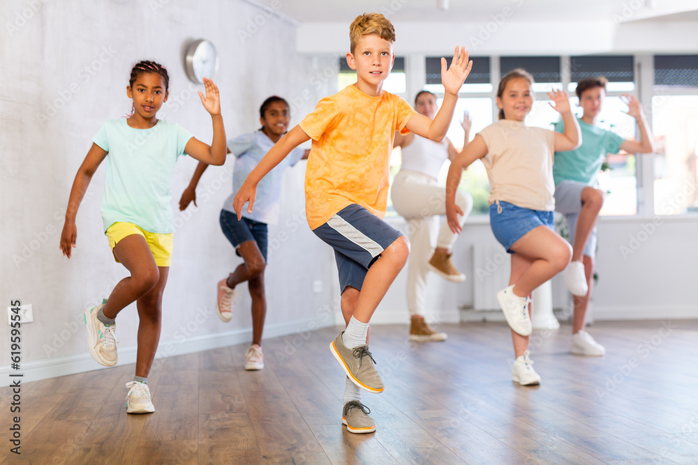 Dynamic little boy training Hip hop dance poses in dancehall with other attendees of dancing courses