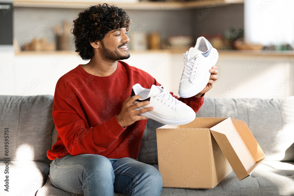 Portrait of happy young indian man unboxing parcel with shoes at home - obrazy, fototapety, plakaty 