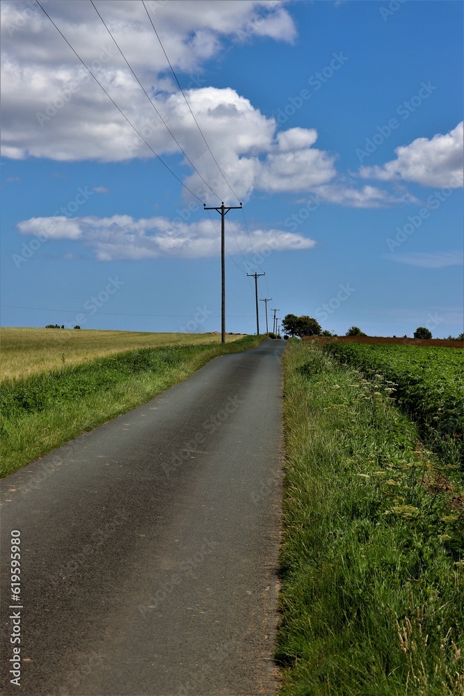 Long country road with telegraph poles against a blue sky with some white clouds