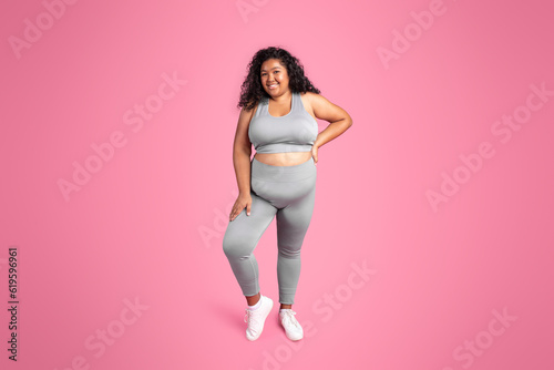 Full length shot of happy black overweight lady in sportswear posing and smiling at camera isolated on pink background