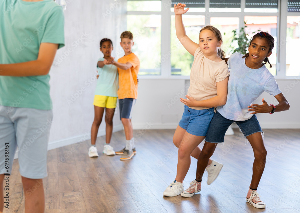 Positive tweenagers, boy and girl dancing slow ballroom dances as couple during choreography lesson with multiethnic group of children..