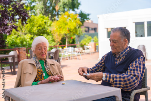 Two elderly people in the garden of a nursing home or retirement home playing cards on a summer morning