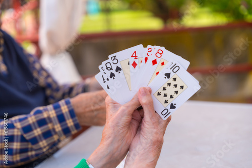 Hands of two elderly people in the garden of a nursing home or retirement home playing cards on a summer morning