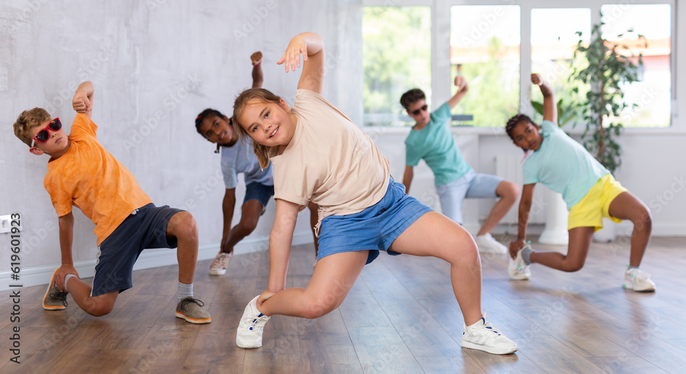 Energetic happy tween girl krumper dancing with group of children in choreographic studio. Concept of self-expression of typical generation Alpha