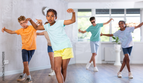 Active preteen girl practicing sport dances with other children in training hall during dancing classes