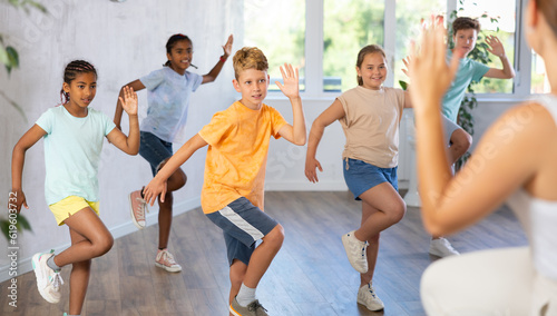 Boy moves to beat of music in dance lesson and repeats movements behind unrecognizable teacher. Multi-racial group of children performs workout in studio