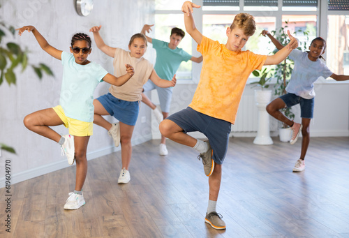 Male child perform choreographic exercises and teaches energetic mobile social dance waacking together with friends. Young girls and guys repeat movements, train in spacious studio unfocused