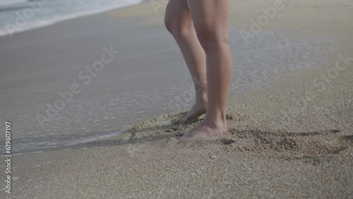 Beautiful girl drowing on the sand. Sea beach. Waves in the background. Leady in the beach. Sea coast. Sunny day. Type 2 photo