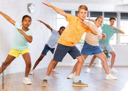 Emotional cheerful tween boy enjoying contemporary dance with group of children  showcasing dabbing move..