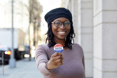 Portrait of smiling woman showing Vote button in city photo