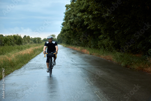 Sportive, young, bearded man, cyclist in uniform, helmet and glasses riding bike on road in chill evening. Calmness. Concept of sport, hobby, leisure activity, training, health, speed, endurance, ad © master1305