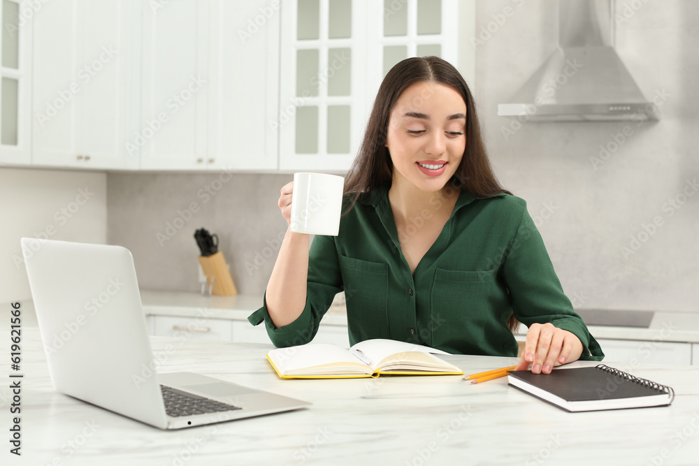 Home workplace. Happy woman opening notebook near laptop at marble desk in kitchen Home workplace. Happy woman opening notebook near laptop at marble desk in kitchen