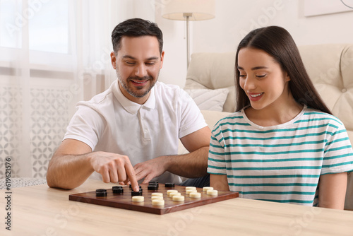 Happy couple playing checkers at table in room